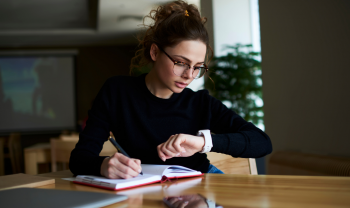 Woman looks at watch, and writes in planner.